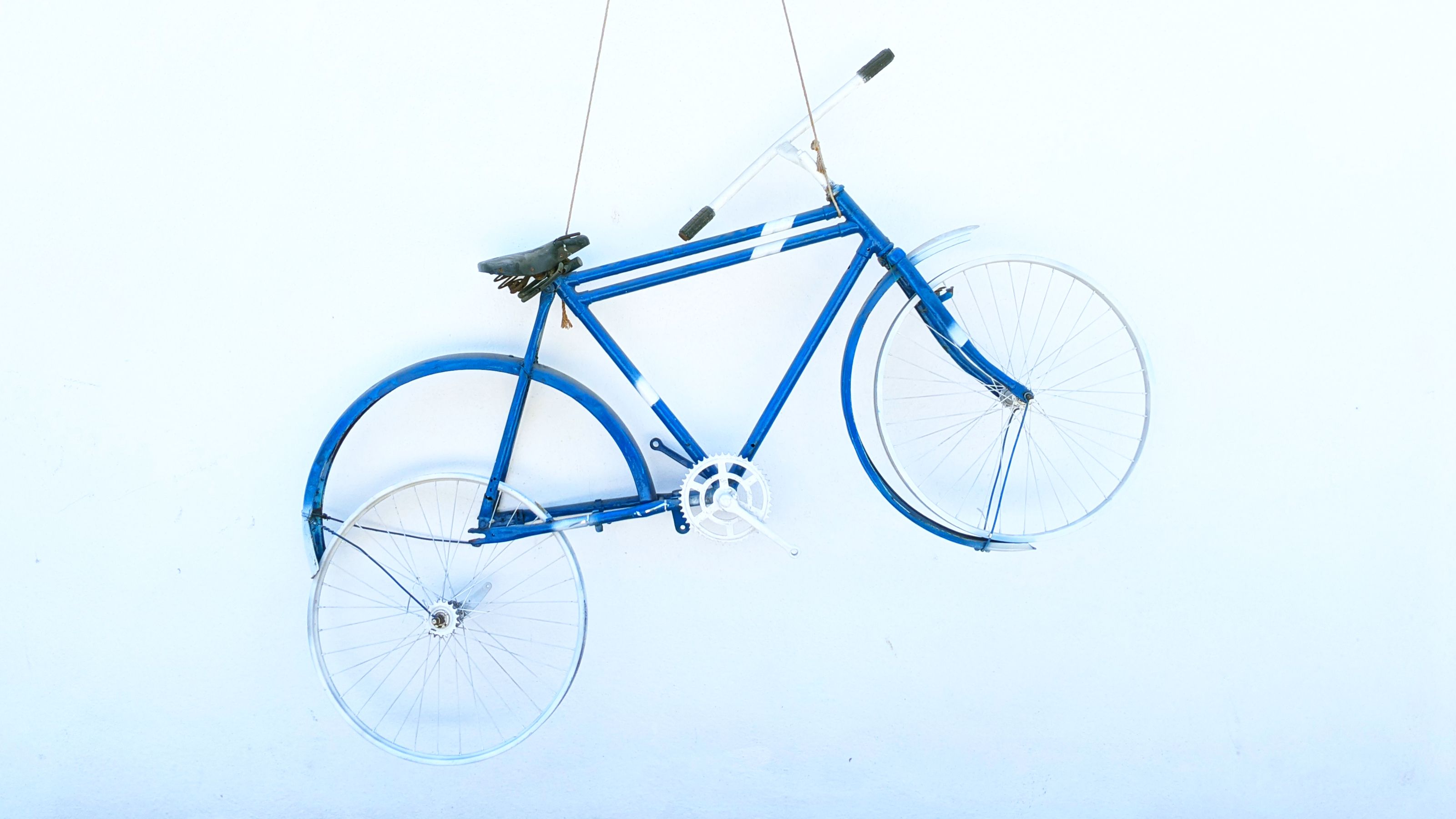 A blue vintage bicycle hanging on a white wall with its wheels parallel to the wall, creating a decorative display.