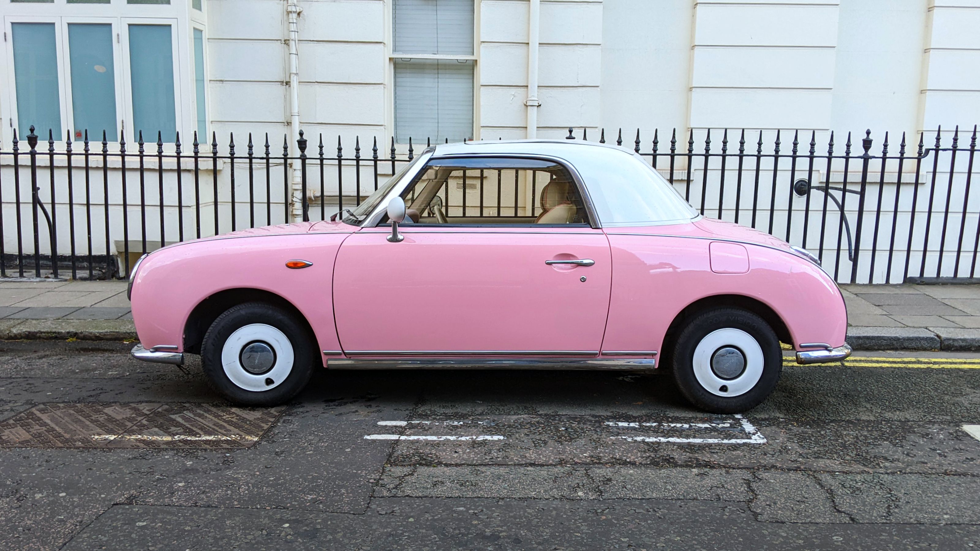A classic style Nissan Figaro in pastel pink parked on a London street.